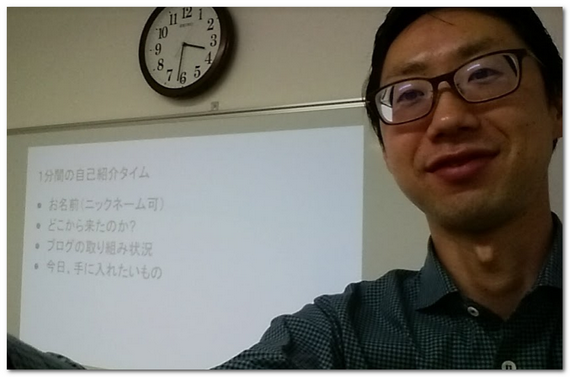 石黒の顔と後ろにホワイトボードと時計がある画像